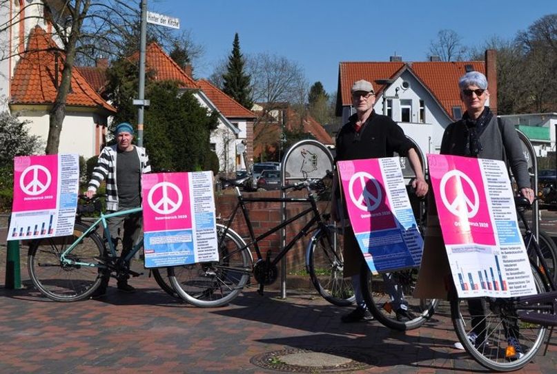 Fritz Böhm, Eckhard Schlöbcke und Anke Beyer (v. li.) präsentieren auf dem Scharmbecker Marktplatz die Ostermarsch-Aktion „Geld für Gesundheit statt für Rüstung.  Foto: eb