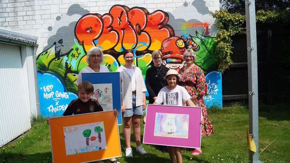 Die stolzen Preisträger:innen vor dem ebenfalls während des Kultursommers entstandenen Grafitto, v. l. n. r.: hinten: Wiebke Müller mit dem Bild von Eva Henjes, Leitung kidsArt, Luna Kolakowski (15), Aiko Drescher (23), Beate Schröder, Leiterin der Schreibwerkstatt, vorne Theo Busch (6) und Frederike Hahn (8). Nicht im Bild: Peter Sperling und Eva Henjes